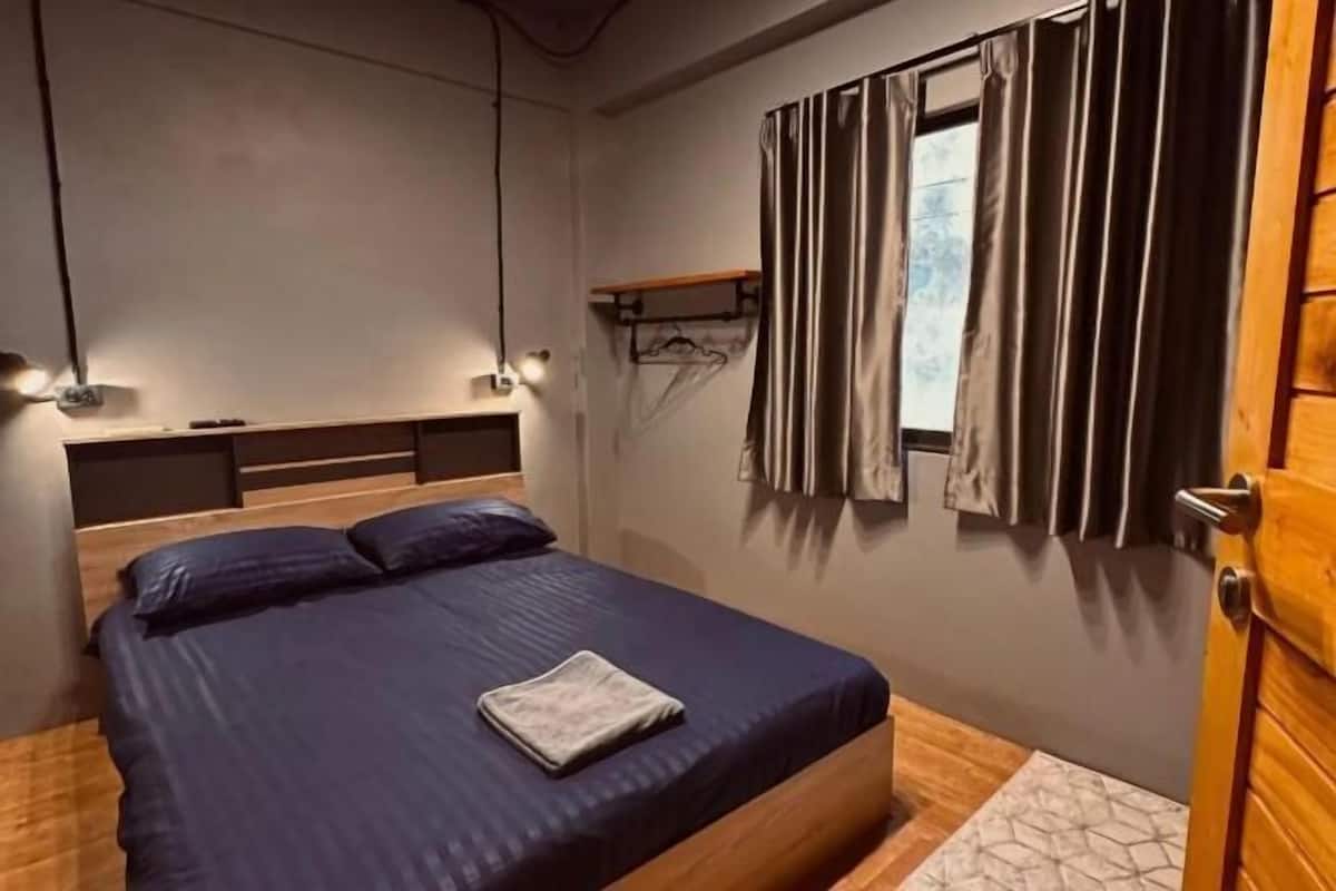 A bedroom with a bed, bedside lamps, a window with curtains, and a wooden door.