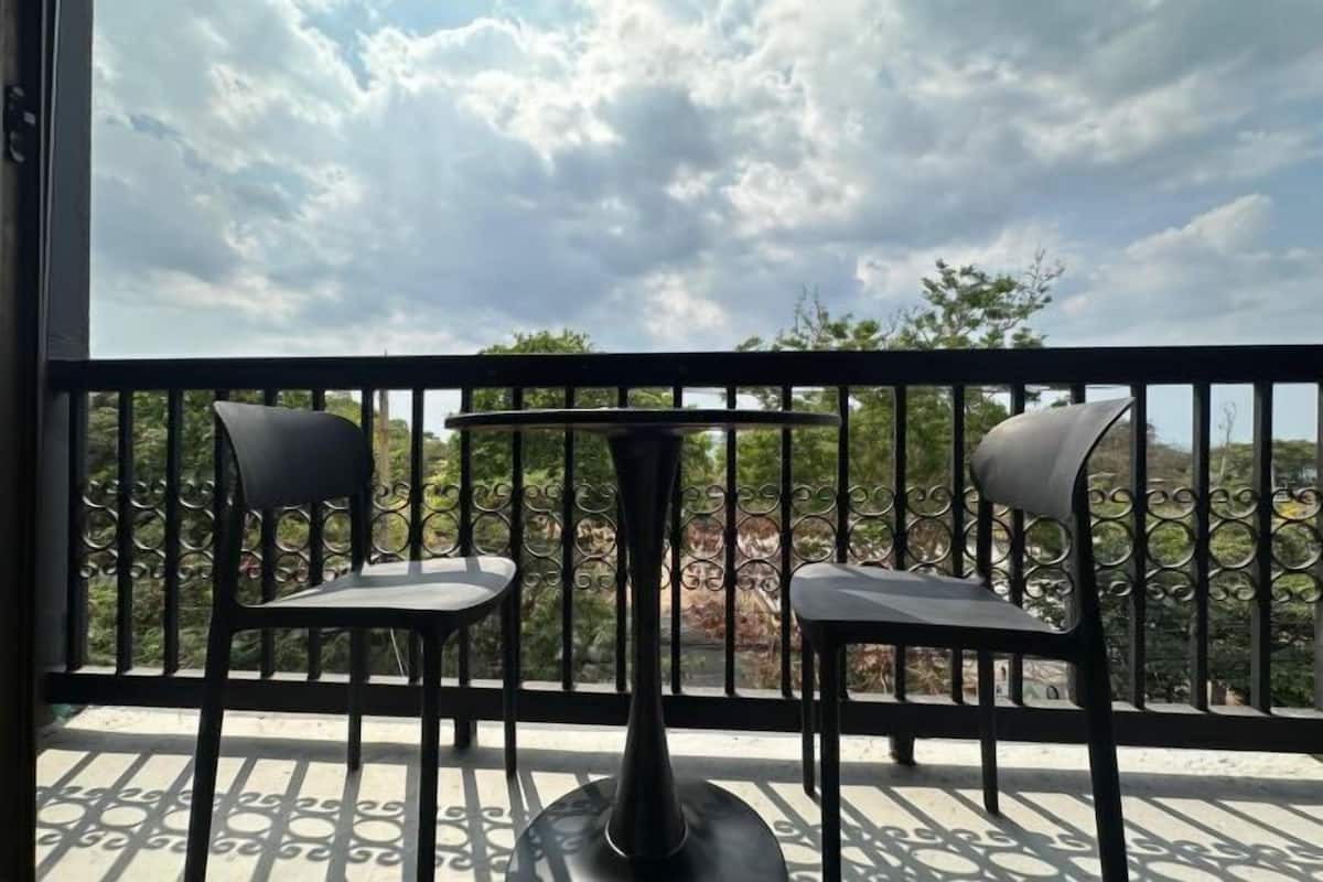 A balcony with two chairs and a table, a metal railing, and a view of trees and hills.