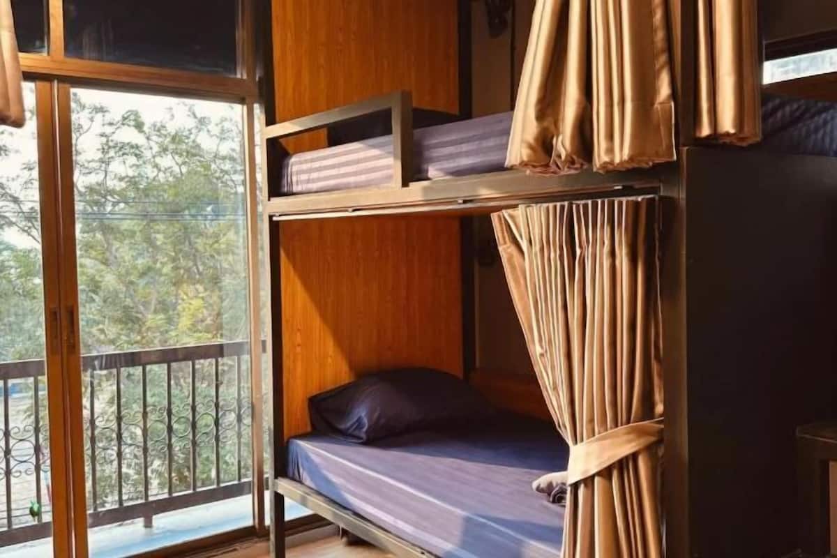 A bunk bed room with a view of trees through a large window.