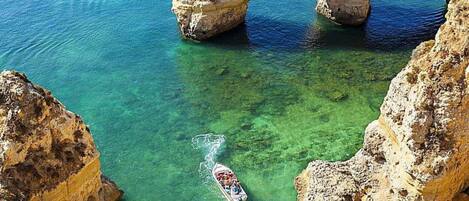 A boat navigating through a clear blue sea with a large rock formation in the background.