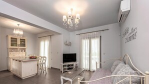 Un salon moderne comprenant un lit, un téléviseur, un coin repas avec une table et des chaises, et une cuisine équipée de meubles et agrémentée d’un lustre.
