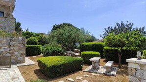 Un jardín bien cuidado con muros de piedra, setos podados y una zona con banco de piedra.