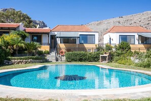 Vue sur un complexe hôtelier depuis la piscine, avec deux bâtiments, une piscine et un paysage montagneux en arrière-plan.