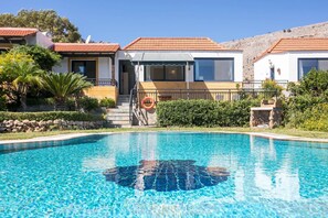 Une piscine avec une eau d’un bleu limpide, une bouée de sauvetage et une maison avec un toit recouvert de tuiles rouges et de grandes fenêtres.