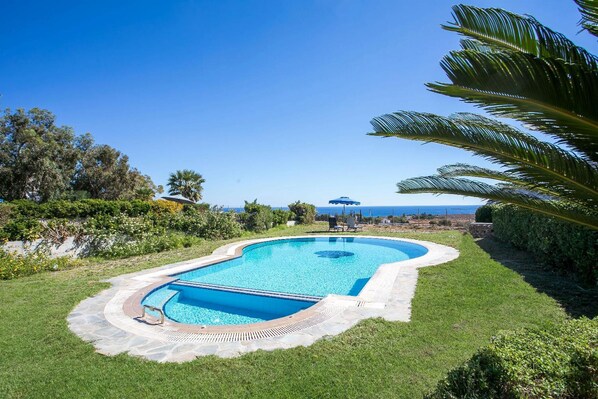 Une piscine à bord incurvé, entourée d’une terrasse en pierre et d’une pelouse.