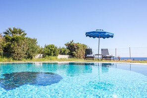 Une piscine d’un bleu éclatant, avec deux chaises longues et un parasol bleu.