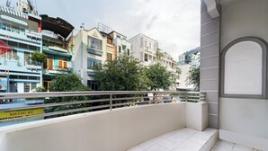 Un balcon doté d’un sol carrelé de carreaux blancs, d’une rambarde en métal et offrant une vue sur des immeubles à plusieurs étages, eux-mêmes dotés de balcons et bordés d’arbres.