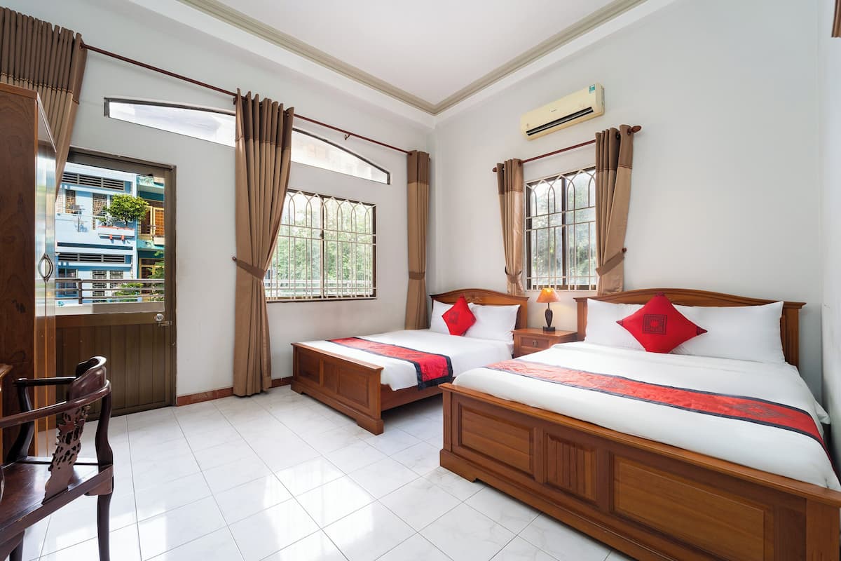 A hotel room with two wooden beds, a wooden chair, a window with curtains, and an air conditioning unit.