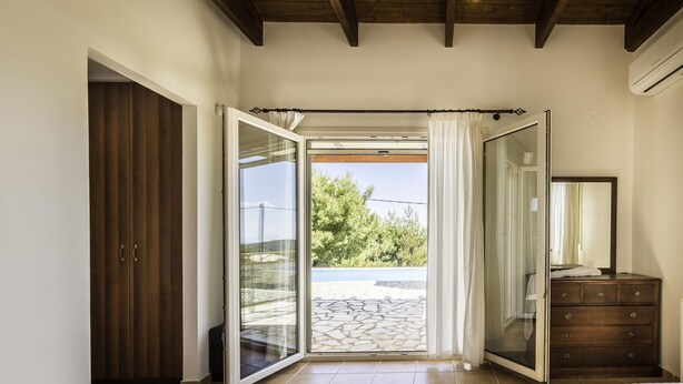 A bedroom with a bed, a dresser, a mirror, and a sliding glass door leading to an outdoor patio. - Villa Eudora in Lefkada (Lefkada)