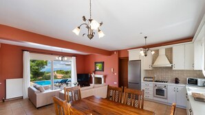 A modern kitchen with white cabinets, a wooden dining table, and a large window overlooking a pool. - Villa Eudora in Lefkada (Lefkada)
