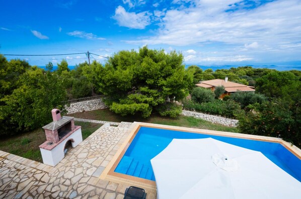 A swimming pool with a stone deck, surrounded by lush greenery and a view of the sea.