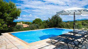 A clear blue swimming pool with lounge chairs and an umbrella, surrounded by greenery and a view of the sea. - Villa Eudora in Lefkada (Lefkada)