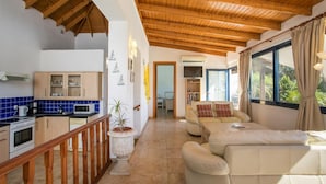A spacious living area with a wooden ceiling, a kitchen with blue tiles, and a view through large windows. - Villa Driftwood in Rhodes (Rhodes)
