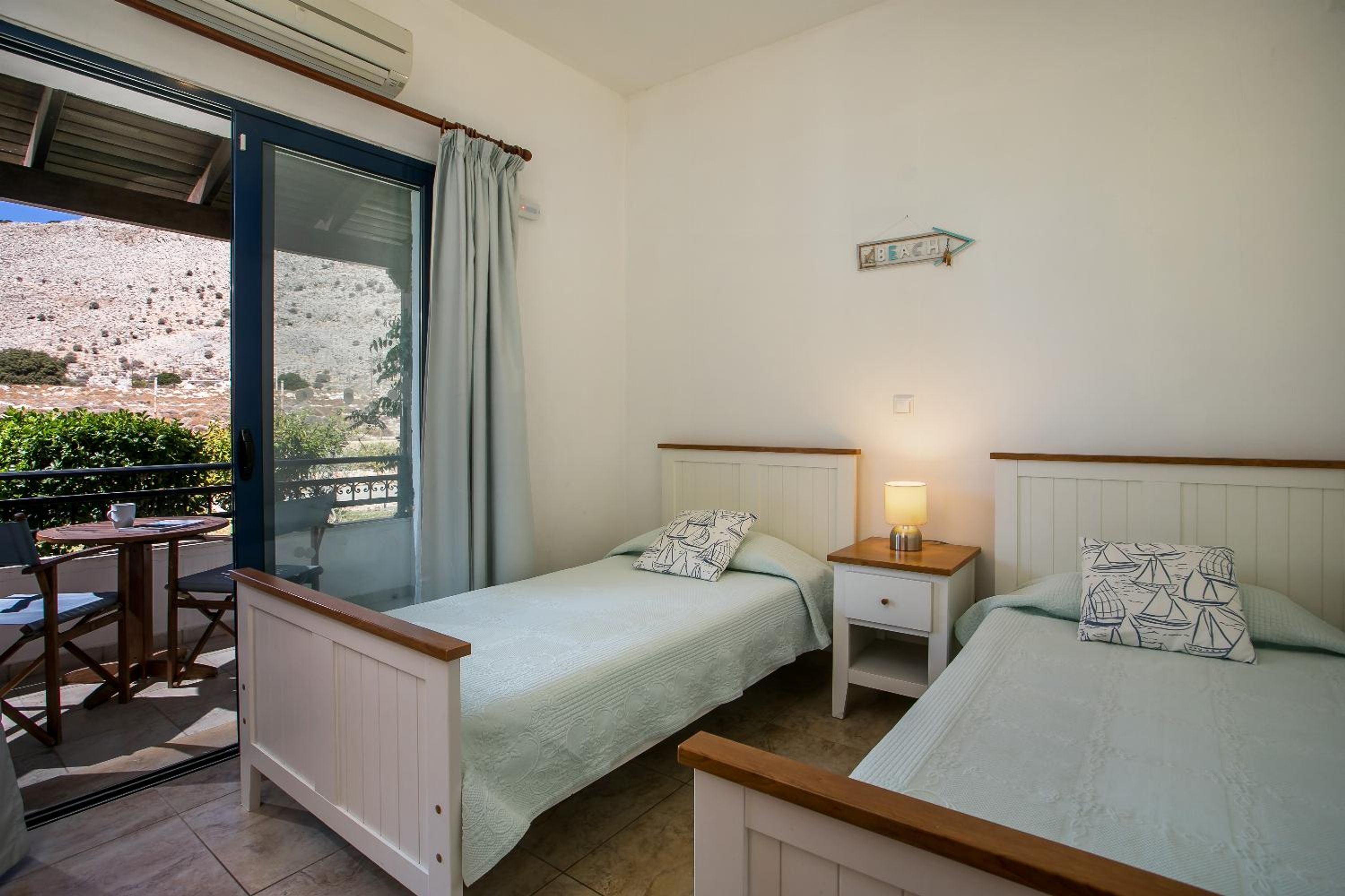 Une chambre avec deux lits, une petite table et une chaise. Il y a une fenêtre donnant sur un paysage rocheux.