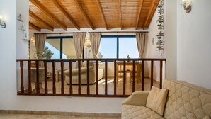 A cozy living room with a beige sofa, wooden ceiling, and a view through a balcony with curtains. - Villa Driftwood in Rhodes (Rhodes)