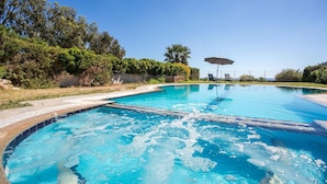 A clear blue swimming pool with a tiled deck, surrounded by lush greenery and a clear sky. - Villa Driftwood in Rhodes (Rhodes)