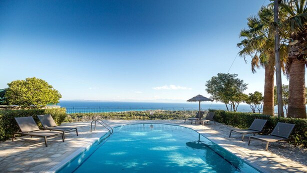 Ein Pool mit Meerblick, umgeben von Liegestühlen und Palmen.