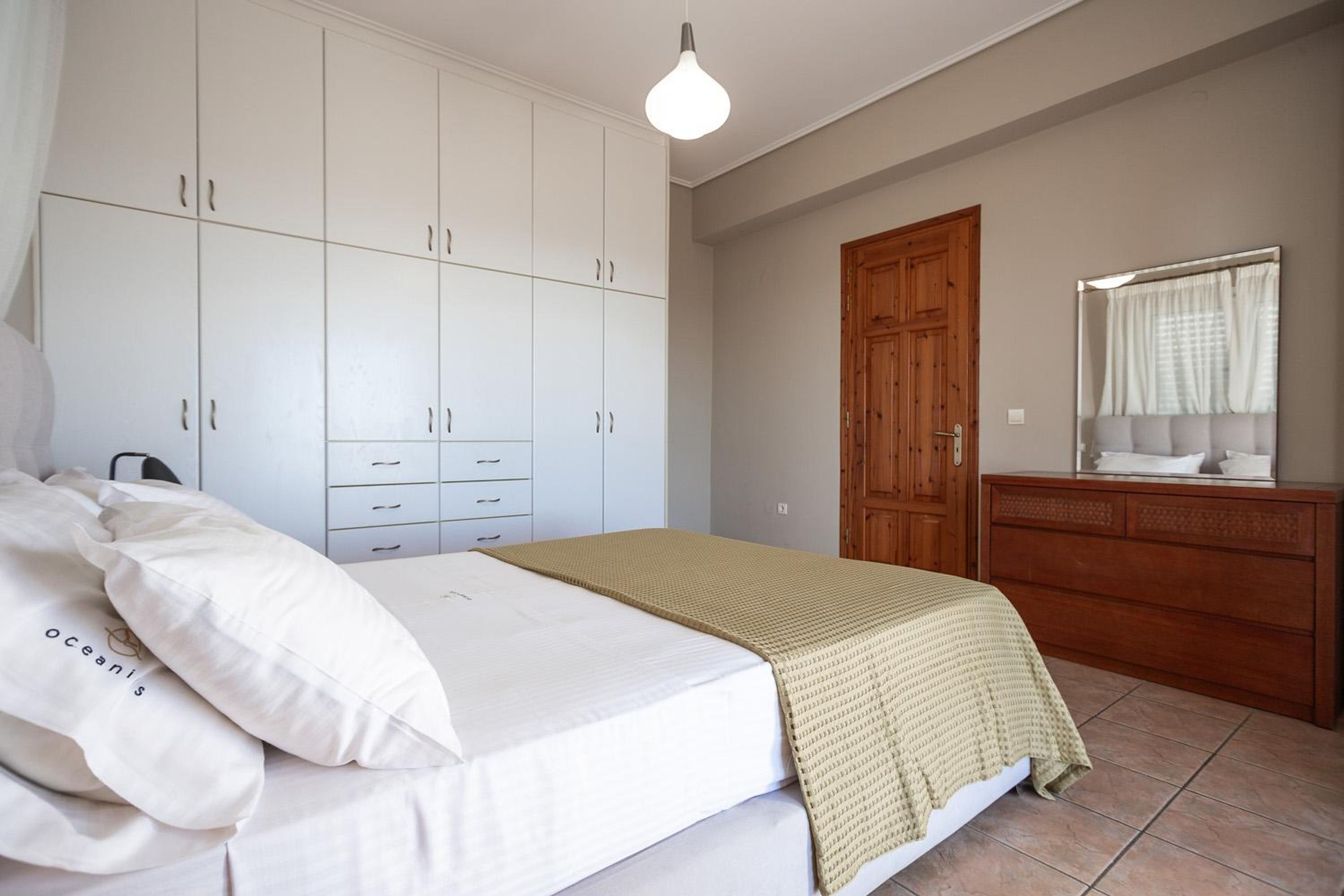 A bedroom with a bed, white wardrobe, wooden dresser, and a mirror.