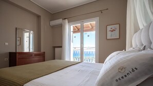 Ein Hotelzimmer mit Bett, einem hölzernen Schminktisch, einem Fenster mit Blick auf einen Balkon und einem gerahmten Bild an der Wand.