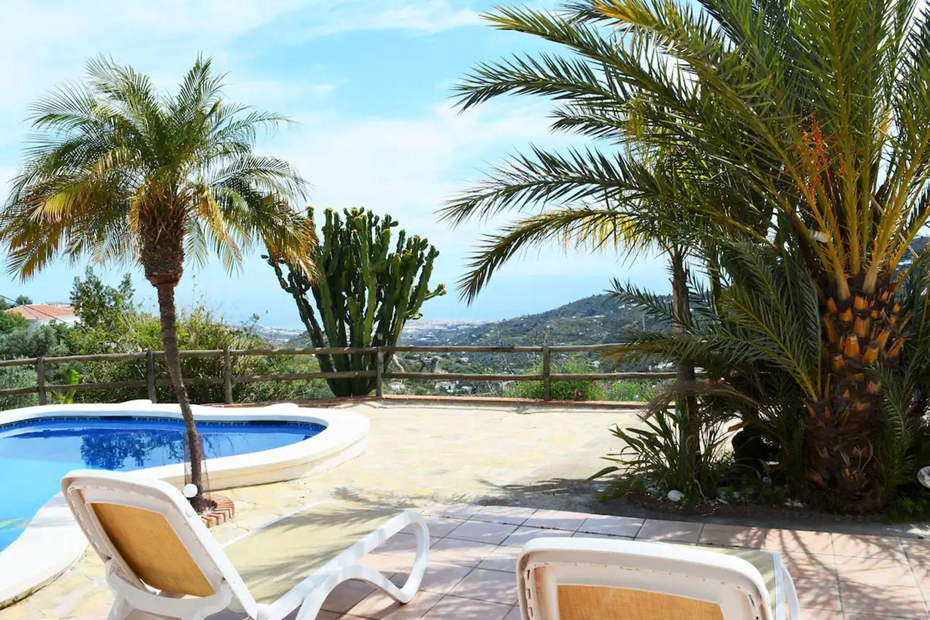 Un espace aménagé au bord de la piscine, avec des chaises longues, des palmiers et une vue sur le paysage.