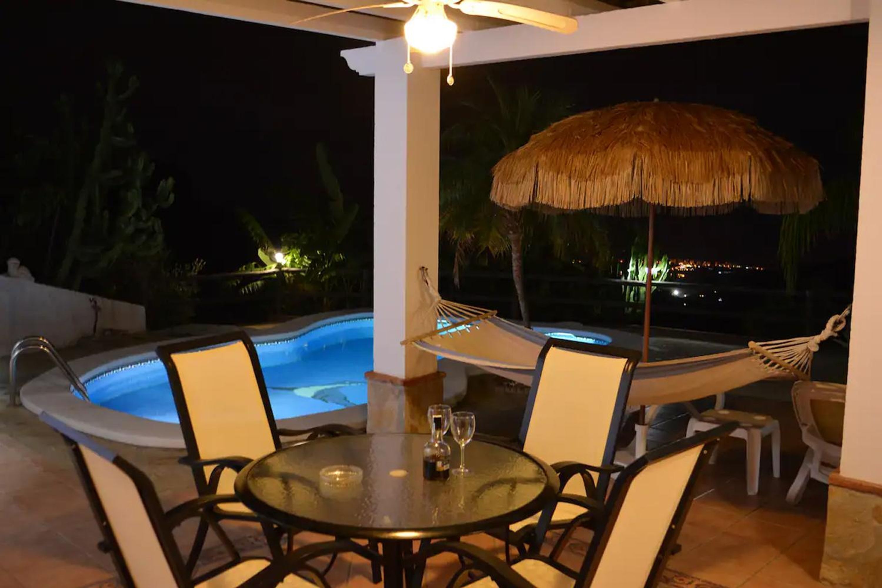 Un espace aménagé au bord de la piscine, avec une table, des chaises, un hamac et un parasol.