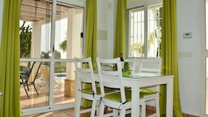A dining area with a glass table and white chairs, a bottle of wine, and green curtains. - Villa Buenavista in C Mpeta (Torrox)