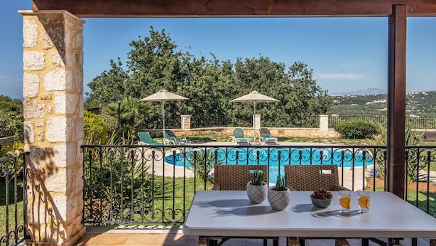 A covered outdoor seating area with a table, chairs, and umbrellas overlooking a swimming pool and lush greenery. - Villa Chloe in Rethymno (Rethymno)