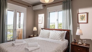 A neatly made bed with white linens and pillows, a bedside table with a lamp, and a balcony with a chair. - Villa Chloe in Rethymno (Rethymno)