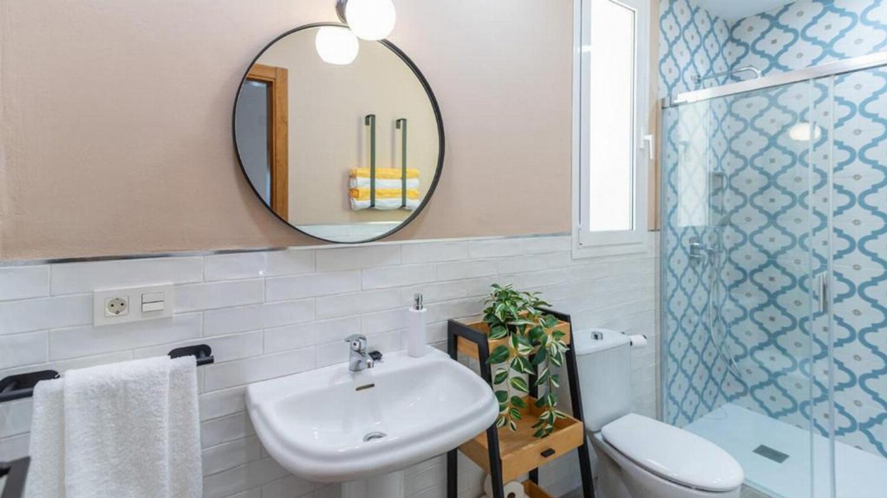 Une salle de bain avec un lavabo blanc, un miroir, des toilettes et une douche dont les carreaux sont décorés de motifs.