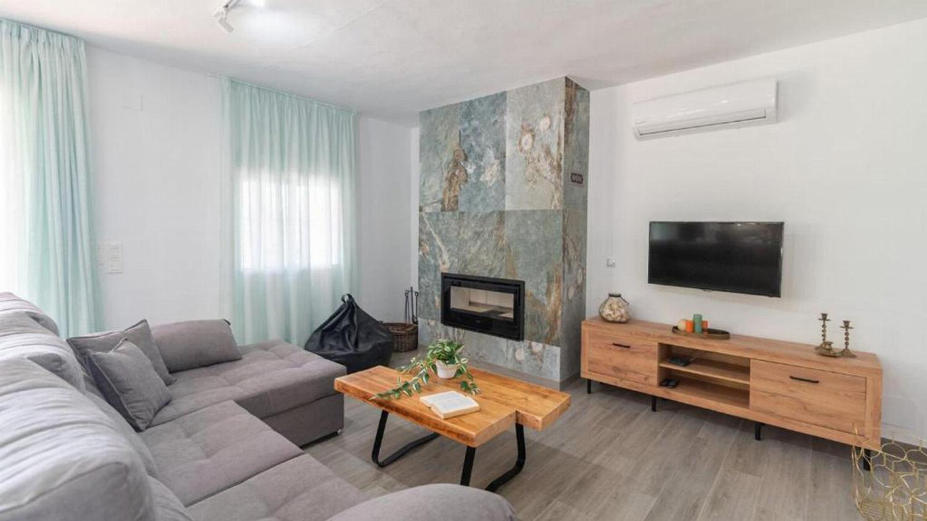 A modern living room with a grey sofa, a wooden coffee table, a fireplace, a TV, and a wooden TV stand.