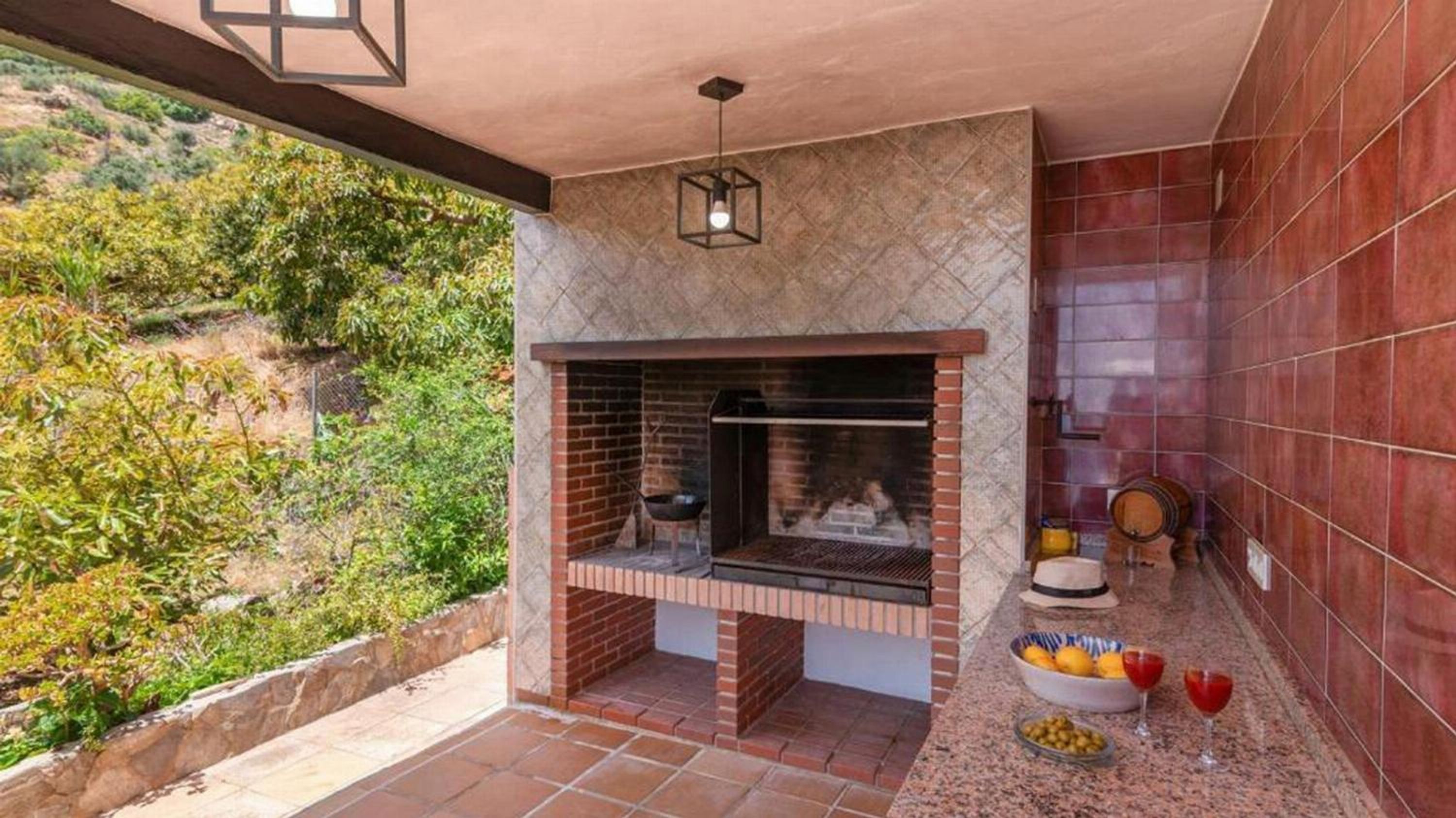 A patio with a brick fireplace, a stone wall, and a view of greenery.