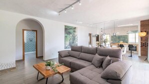 Una sala de estar moderna con un sofá modular, una mesa de centro de madera y un comedor al fondo.
