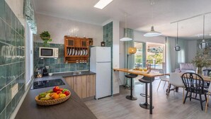 Una cocina moderna con microondas, refrigerador y armarios de madera. Hay un frutero en la encimera y un comedor con mesa y sillas.