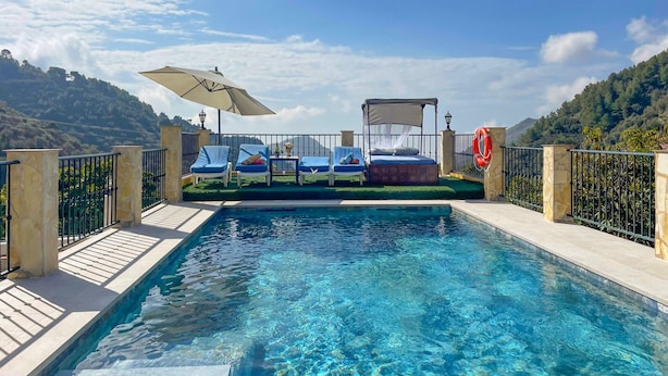 Un área de piscina con una cama, sillones y una sombrilla.