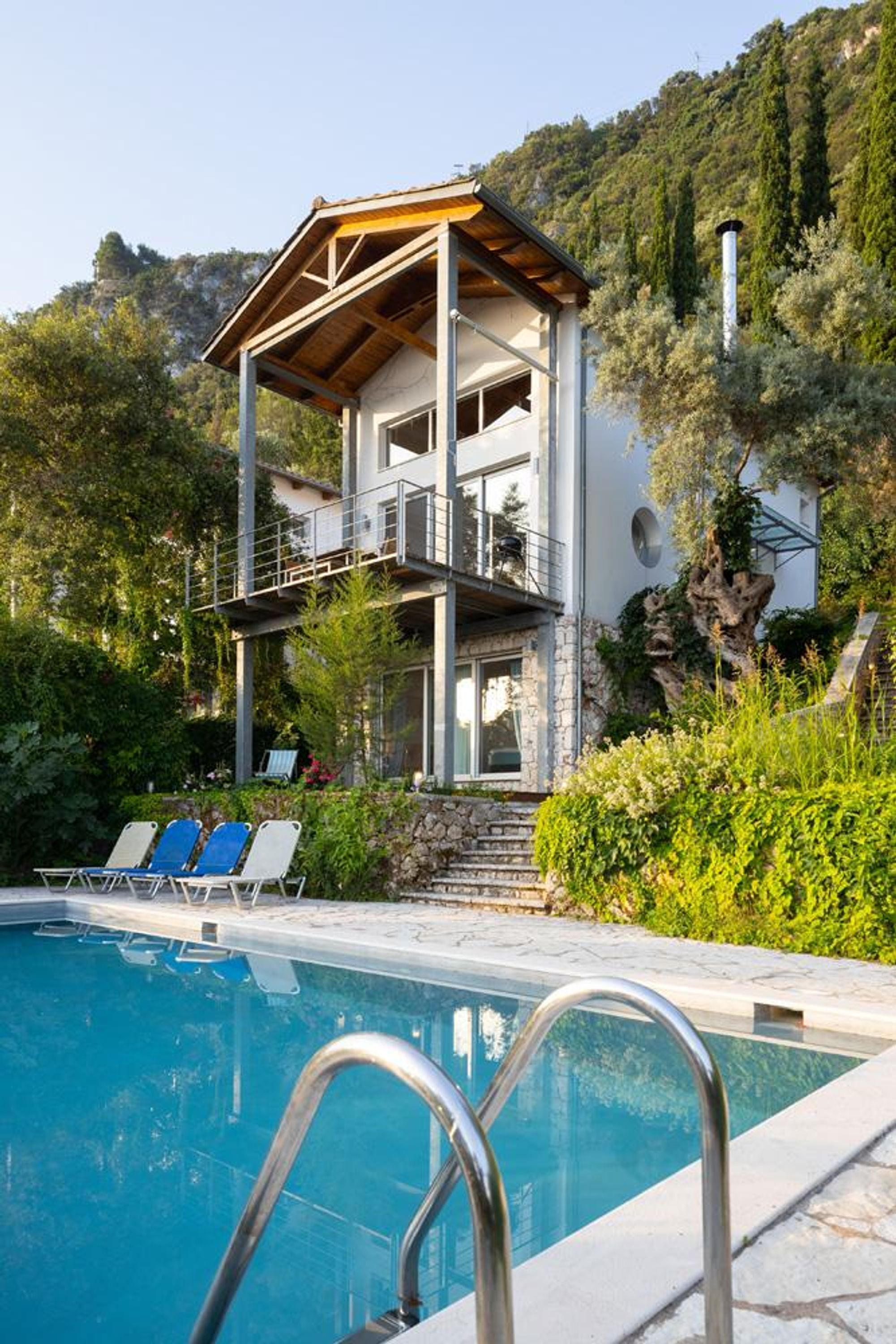 A modern two-story house with a pool, surrounded by lush greenery and a mountainous backdrop.
