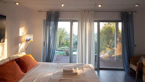 Et moderne hotelværelse med en stor seng, udsigt til haven gennem en skydedør og en fletstol ved vinduet.