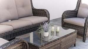 Un conjunto de sofá y sillones de mimbre con una mesa de centro de vidrio, una planta en maceta y velas.