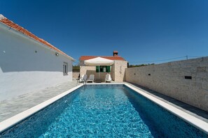 A swimming pool with a stone wall and a white building with a red roof. - Villa Iva in Donje Ra Tane (Sveti Filip i Jakov)