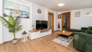 Una sala de estar moderna con un televisor de pantalla plana, un sofá verde, una mesa de centro de madera y una planta en maceta.