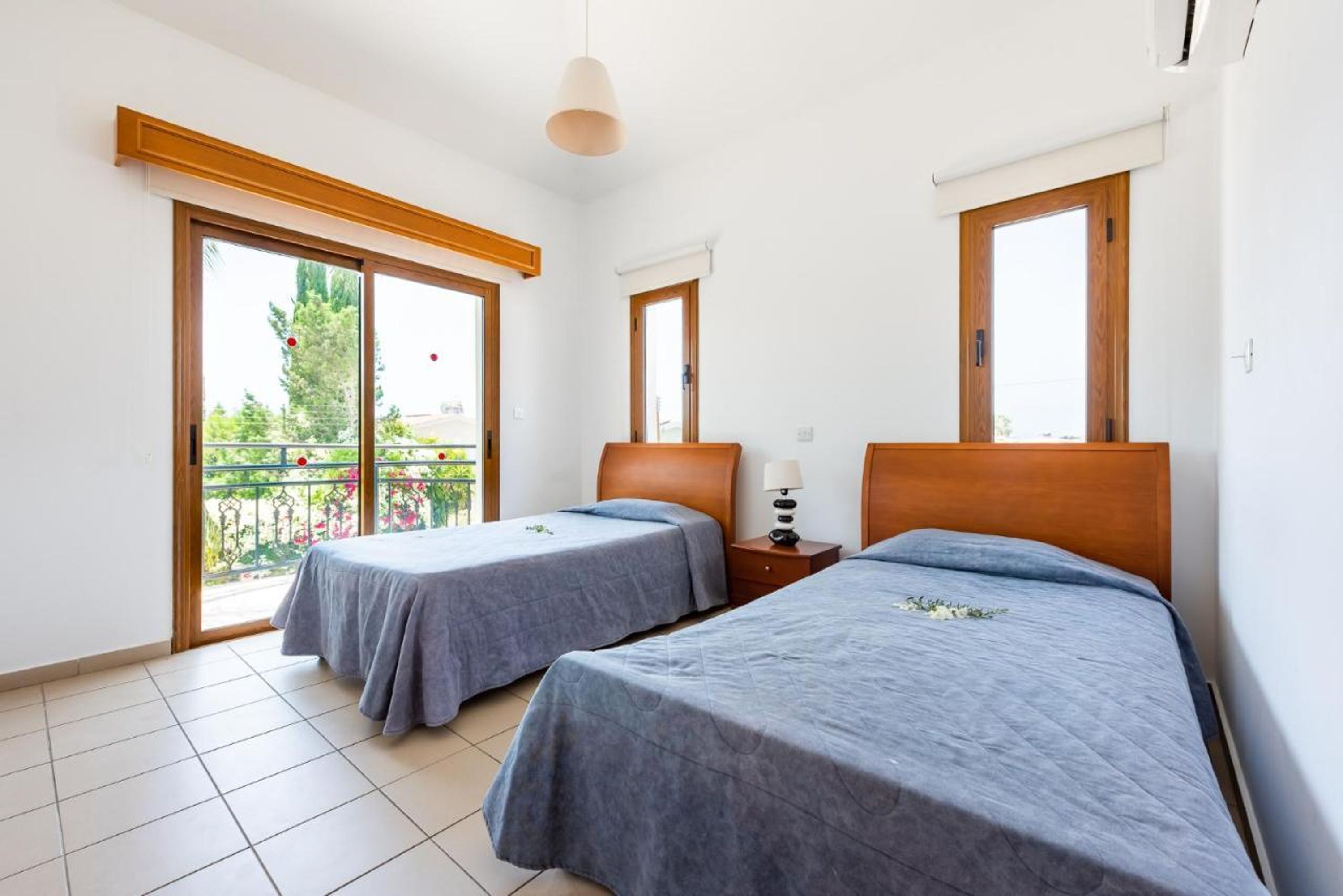 A room with two beds, a small table with a lamp, and a balcony with a railing.