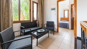 Una habitación con sofá, dos sillones, una mesita con un plato, cama y espejo.