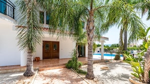 Una casa con piscina, palmeras y patio con baldosas.