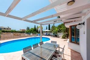 A covered outdoor area with a pool, a table with chairs, and a view of the surrounding landscape. - Villa Corallina in Peyia (Pegeia)