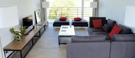 Una sala de estar moderna con un sofá gris, cojines rojos, una mesa de centro y un televisor sobre un mueble de madera.