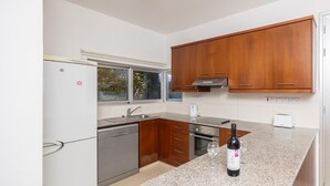 A modern kitchen with wooden cabinets, a stainless steel refrigerator, a dishwasher, a built-in oven, and a granite countertop.