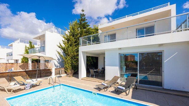 A modern building with a pool, outdoor seating, and a view of a cityscape.