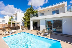 Ein modernes Gebäude mit Pool, Sitzgelegenheiten im Freien und Blick auf eine Stadtlandschaft.