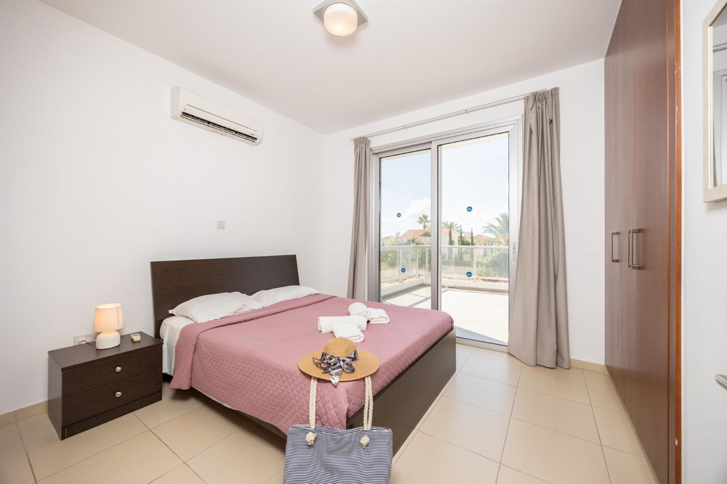 Quarto com cama, mesa de cabeceira, luminária e vista do exterior através de uma porta de correr.
