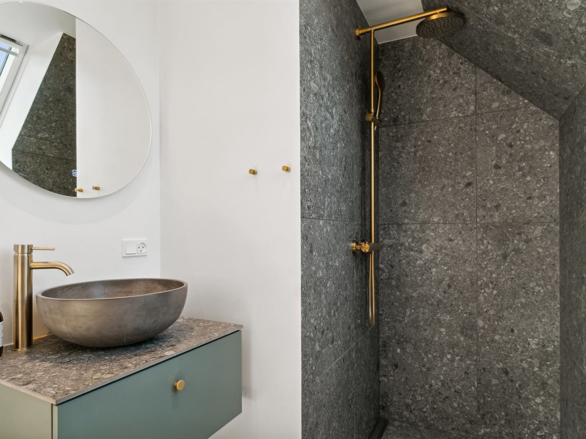 Une salle de bain avec un miroir rond, un lavabo sur colonne, un robinet doré et une douche dotée d’un pommeau de douche doré.