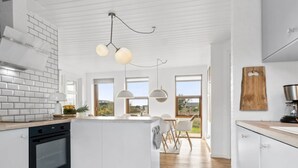 Une cuisine moderne avec des meubles blancs, un îlot central et des luminaires suspendus.